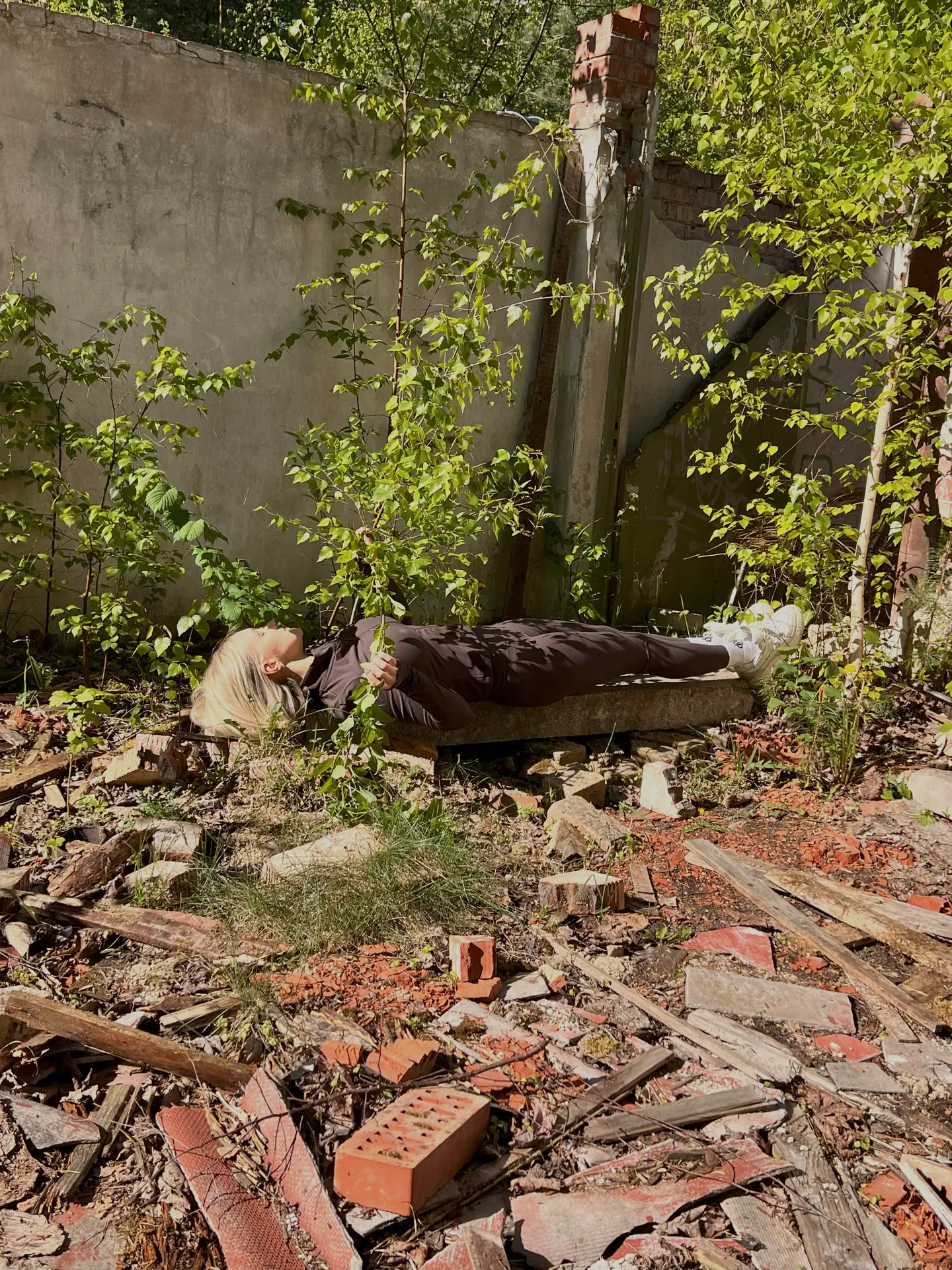 A person lying on a concrete slab among branches and rubble.